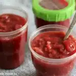 Homemade rhubarb freezer jam in a jar with fresh rhubarb stalks.
