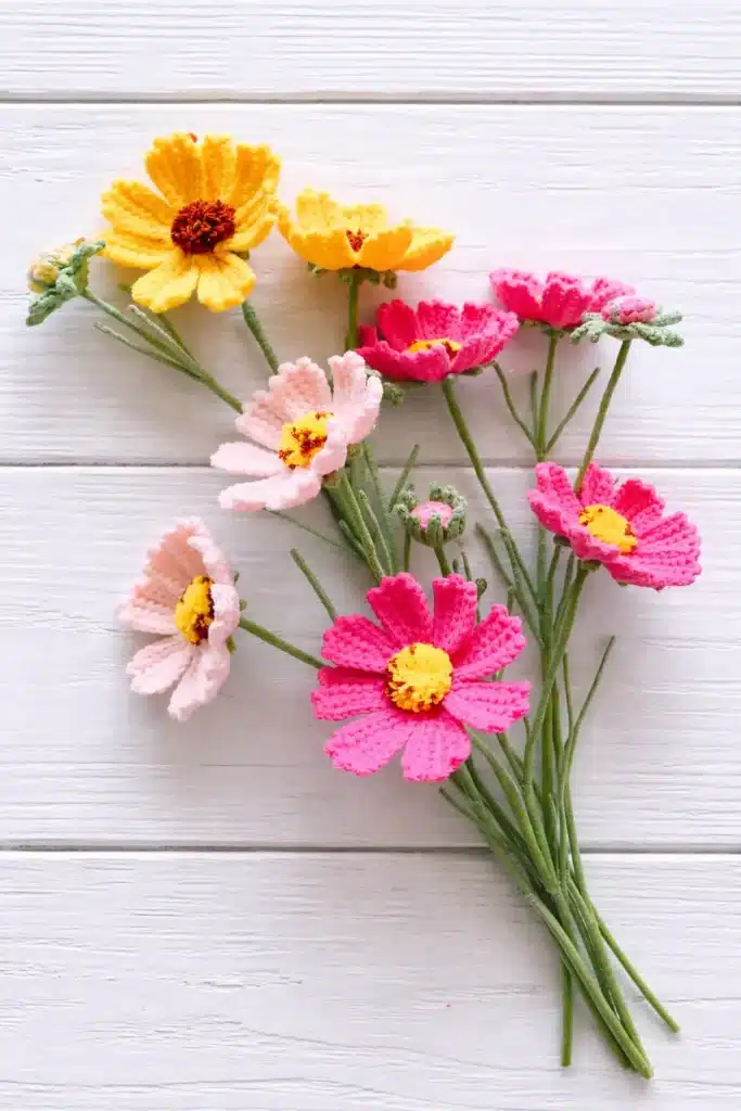 Crochet cosmos flower bouquet pattern with pink, blush, and yellow flowers on a white wooden background